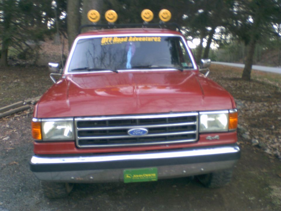 Red Ford pickup truck with smiley face lights on roof rack and 'Off Road Adventures' sticker on windshield