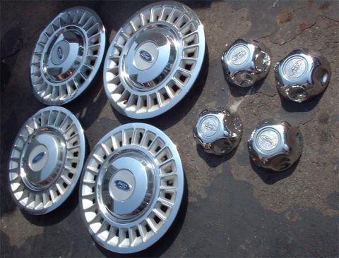 1997 Ford Crown Victoria - Collection of Ford hubcaps and center caps displayed on a dark, rough surface.
