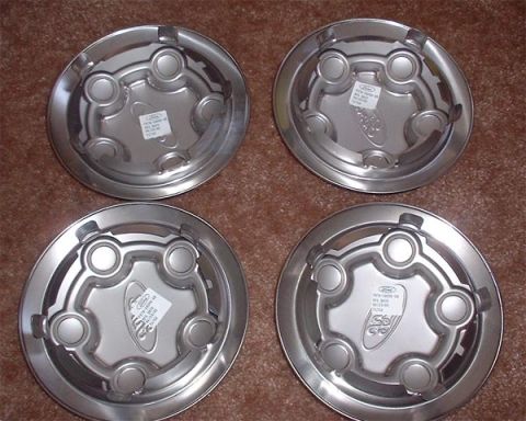 1997 Ford Crown Victoria - A collection of four Ford hubcaps are displayed on a textured brown surface.