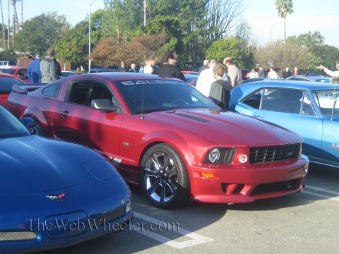 1985 Ford Mustang - A red Saleen Mustang is parked at a car show with other vehicles and people around.