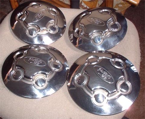 1997 Ford Crown Victoria - Four chrome Ford hubcaps are displayed on a textured surface.