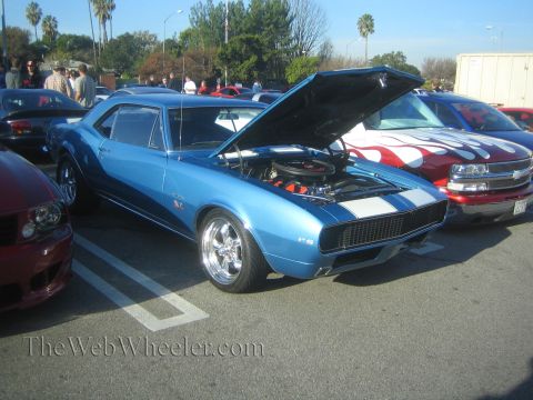 1985 Ford Mustang - A blue 1967 Chevrolet Camaro RS is displayed at a car show with its hood open, parked next to a red truck with flame graphics.