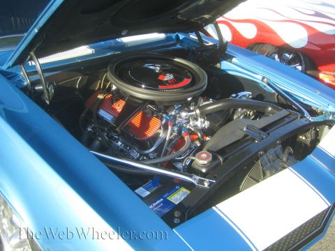 1985 Ford Mustang - The engine bay of a blue 1969 Chevrolet Camaro is open, revealing its V8 engine and chrome details.
