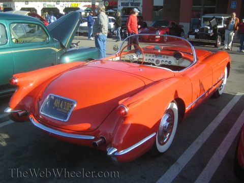 1985 Ford Mustang - Red 1955 Chevrolet Corvette convertible parked at a car show, with other vehicles visible.