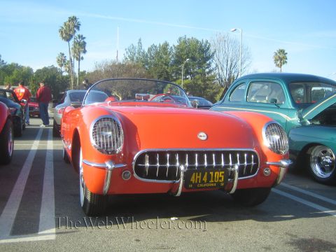 1985 Ford Mustang - A bright orange 1955 Chevrolet Corvette convertible is parked at a car show, displaying its iconic chrome grille and front end.
