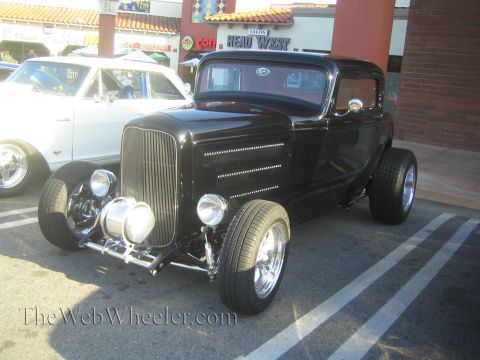 1985 Ford Mustang - A black hot rod coupe is parked next to a white car at a car show.