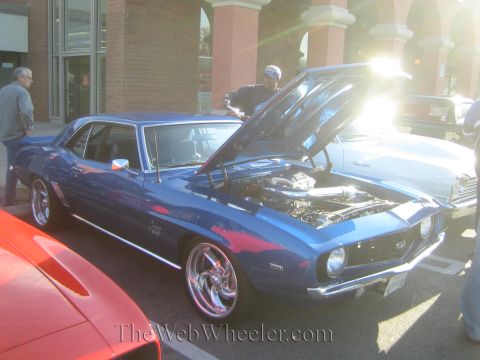 1985 Ford Mustang - A blue 1969 Chevrolet Camaro SS is displayed with its hood open at a car show, revealing the engine and chrome wheels.