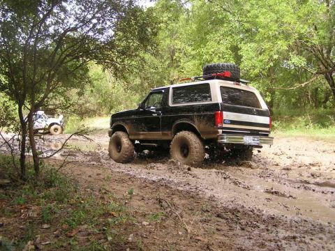 1996 Ford Bronco - A black and tan Ford Bronco navigates a challenging muddy off-road path.