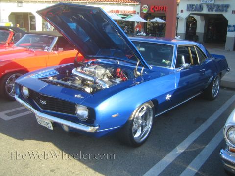 1985 Ford Mustang - A blue muscle car is parked at a car show with its hood open, revealing a powerful engine and turbocharger.