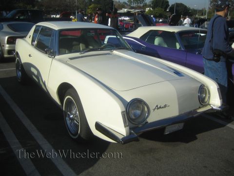 1985 Ford Mustang - A white Avanti is displayed at a car show alongside other vehicles.