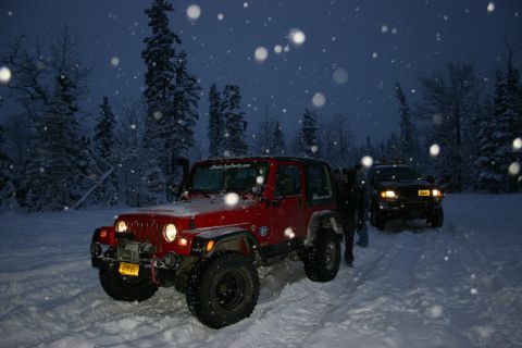 2003 Jeep TJ - Two off-road vehicles navigate a snowy path through a forest under a dark, snowy sky.