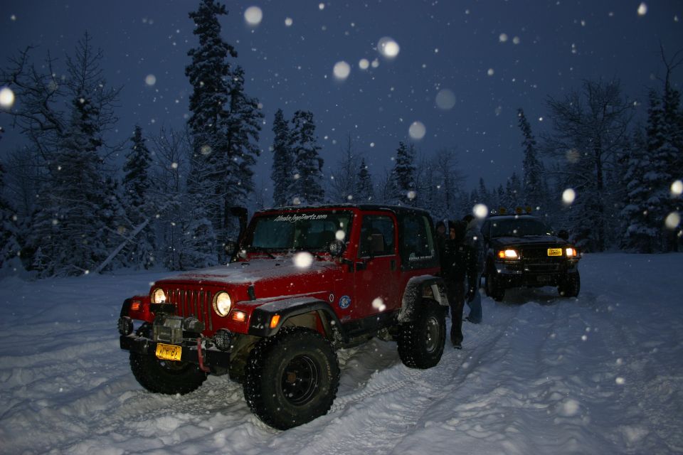 Red Jeep Wrangler with snorkel in snowy forest at dusk, another vehicle behind