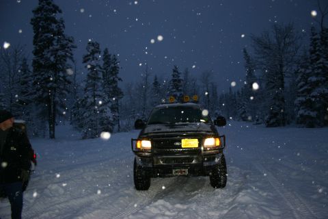 2003 Jeep TJ - A black Ford F-150 is parked on a snowy road surrounded by trees as snow falls.