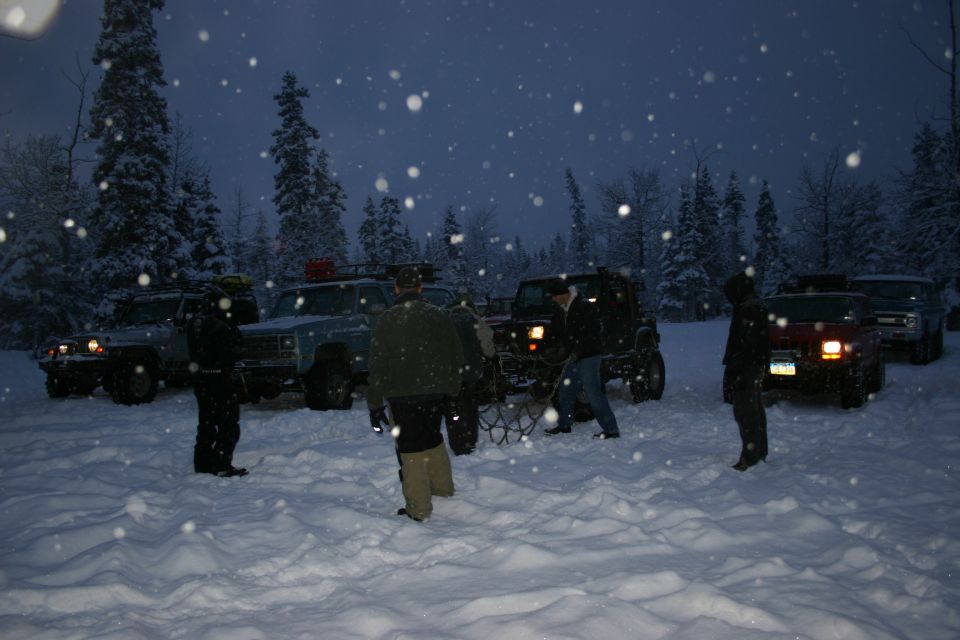 Jeep TJ in snow, front 3/4 view, headlights on, with people around it
