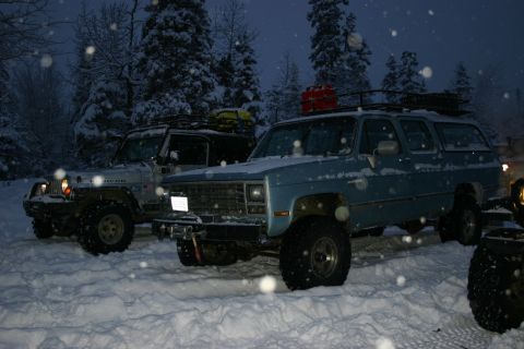 2003 Jeep TJ - Two modified off-road vehicles are parked in a snowy landscape during snowfall.