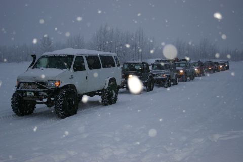 2003 Jeep TJ - A convoy of modified off-road vehicles travels through a snowy landscape during snowfall.