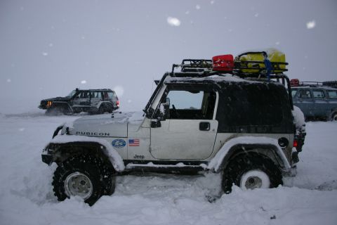 2003 Jeep TJ - Multiple vehicles navigate a snowy landscape, with one Jeep Wrangler prominently featured in the foreground.