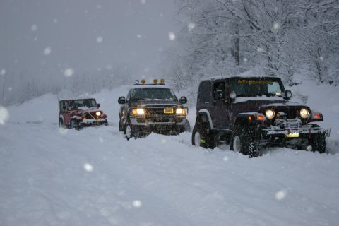 2003 Jeep TJ - Three off-road vehicles navigate a snowy path during a blizzard.