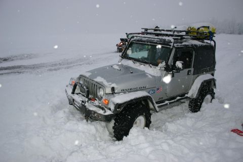 2003 Jeep TJ - A silver 2003 Jeep Wrangler Rubicon is partially buried in snow, with another vehicle visible in the background.