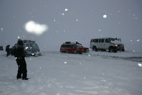 2003 Jeep TJ - Multiple vehicles struggle in heavy snowfall, with a red SUV appearing stuck in the snow.
