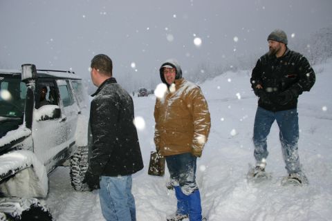 2003 Jeep TJ - People stand around off-road vehicles in a snowy landscape during a snowstorm.
