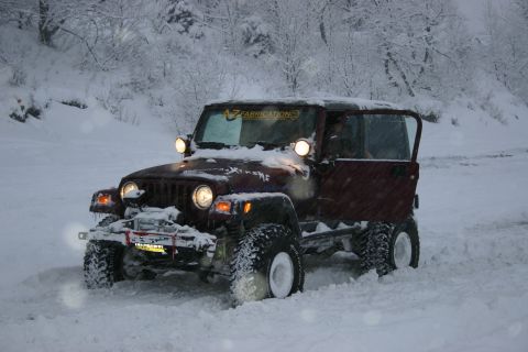 2003 Jeep TJ - A red 2003 Jeep TJ navigates a snowy landscape with its door open and a winch mounted on the front bumper.