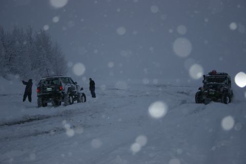 2003 Jeep TJ - Two off-road vehicles and people in a snowy landscape during snowfall.