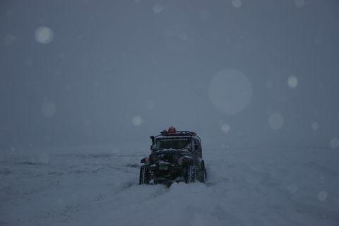 2003 Jeep TJ - A dark Jeep TJ navigates through deep snow under a cloudy sky with falling snow.
