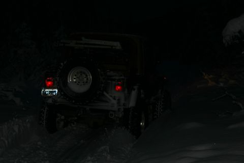 2003 Jeep TJ - 2003 Jeep TJ navigating snowy terrain at night, rear lights illuminated.