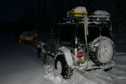 2003 Jeep TJ - A silver Jeep Wrangler, possibly a 2003 model, is stuck in deep snow with another vehicle visible in the background.