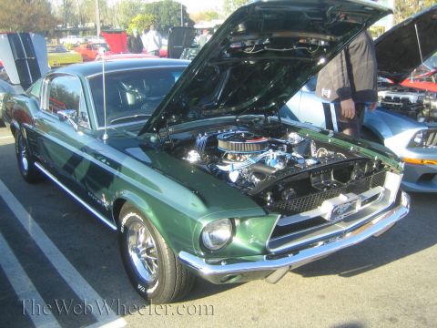 1985 Ford Mustang - A green 1967 Ford Mustang Fastback is displayed with its hood open at a car show.