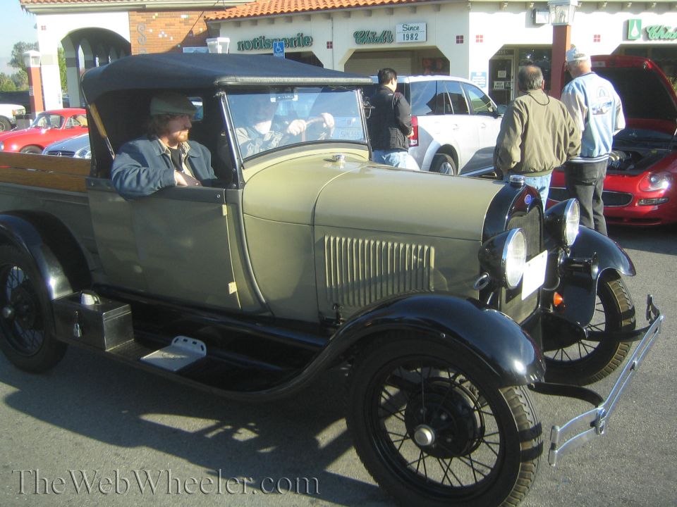 1929 Ford Model A pickup truck with black soft top and tan body, parked at a car show