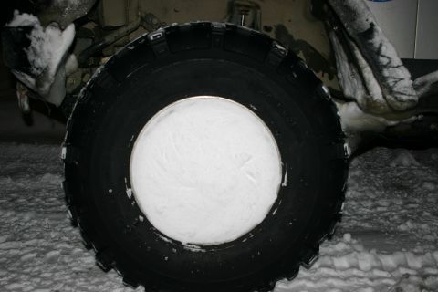 2003 Jeep TJ - A tire packed with snow is shown, with parts of a vehicle visible around it.