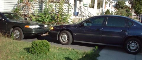 1997 Ford Crown Victoria - Two sedans are parked in front of a house, one dark green and the other dark blue.