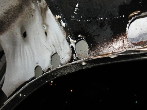 1994 Ford Bronco - Extreme close-up of body repair in progress: a bare white patch panel lapped over a black painted panel edge, with a row of plug-weld holes…