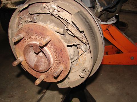 1996 Ford Bronco - Rear drum brake assembly showing wear and rust on components. A hydraulic jack supports the vehicle.