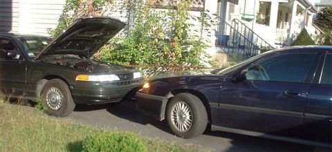 1997 Ford Crown Victoria - Two sedans are parked on a driveway, one with its hood up.