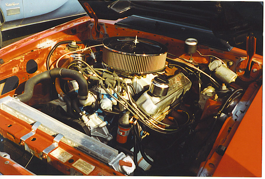Engine bay of a red car, likely a Fox body Mustang. Shows V8 engine, air filter, radiator, and hoses