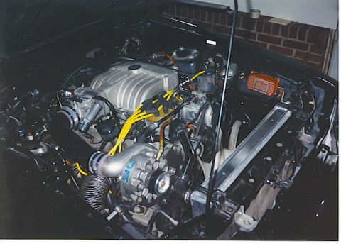 1992 Ford Mustang - The engine bay of a black 1986 Ford Mustang GT shows a supercharger and yellow spark plug wires.