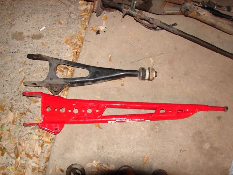 1996 Ford Bronco - Two suspension control arms, one red and one black, are laid out on a concrete surface with fallen leaves.