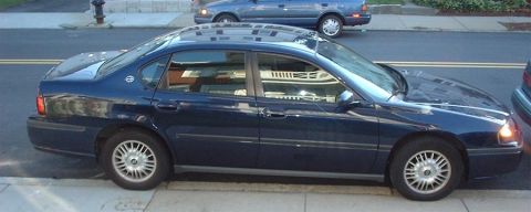 1997 Ford Crown Victoria - A dark blue sedan is parked on the street, with another vehicle visible in the background.