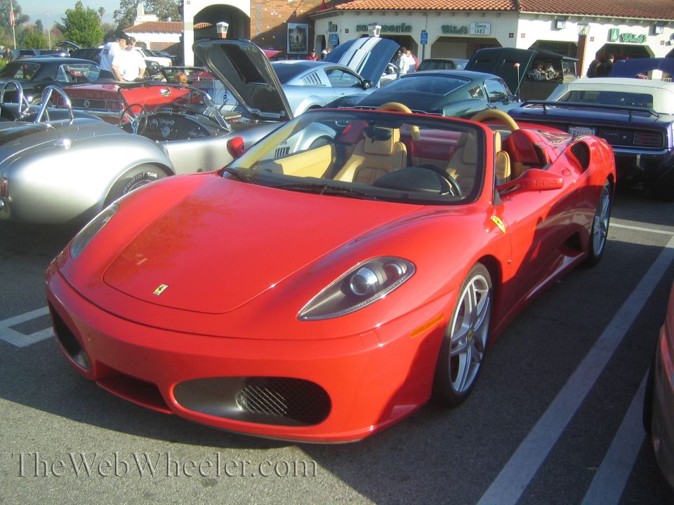 Red convertible sports car parked at a car show. Other cars are visible in the background