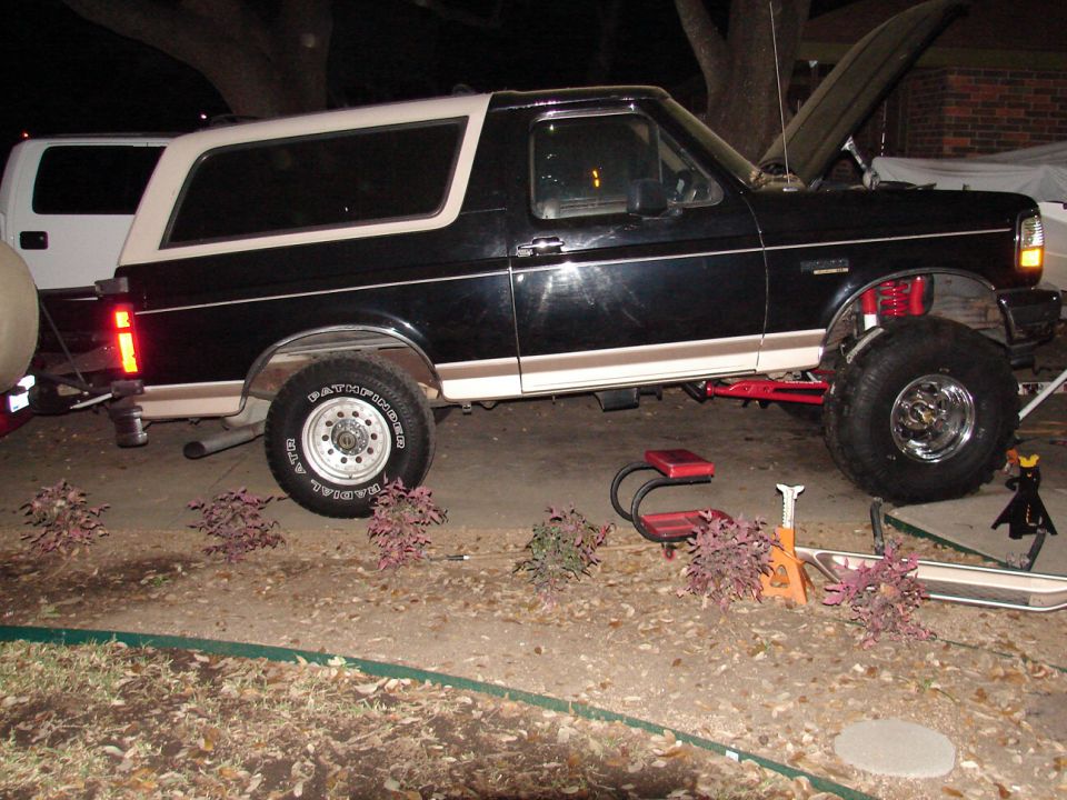 Black and white Ford Bronco on jack stands at night, red front coils and Pathfinder ATR tires