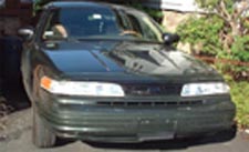 1997 Ford Crown Victoria - A dark green sedan is parked outdoors, showing its front grille and headlights.