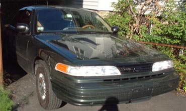 1997 Ford Crown Victoria - A dark green Ford Crown Victoria is parked outside, partially in shadow, with a watermark on the lower right.