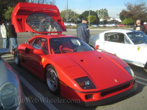 1985 Ford Mustang - A red Ferrari F40 is displayed with its doors open at a car show, alongside a white Ford Mustang GT350.