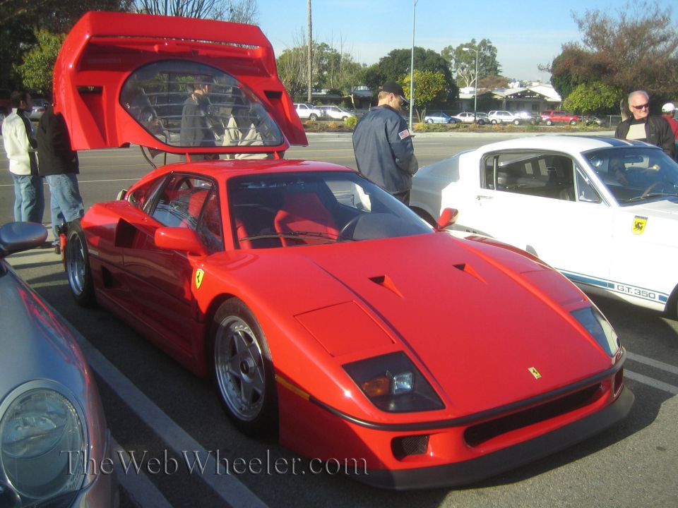 Red Ferrari F40 with doors open, parked next to a white Ford Mustang GT350