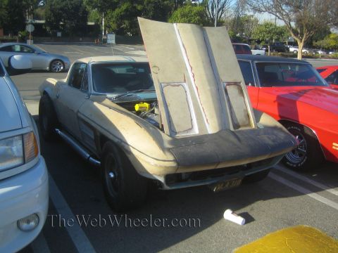 1985 Ford Mustang - A modified 1965 Chevrolet Corvette with its hood open sits at a car show next to a red car.