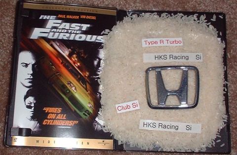 1997 Ford Crown Victoria - A Honda emblem and movie case are displayed on a bed of rice, with various labels indicating car parts.
