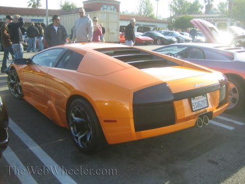 1985 Ford Mustang - An orange Lamborghini is parked at a car show, displaying its distinctive rear end and custom wheels.